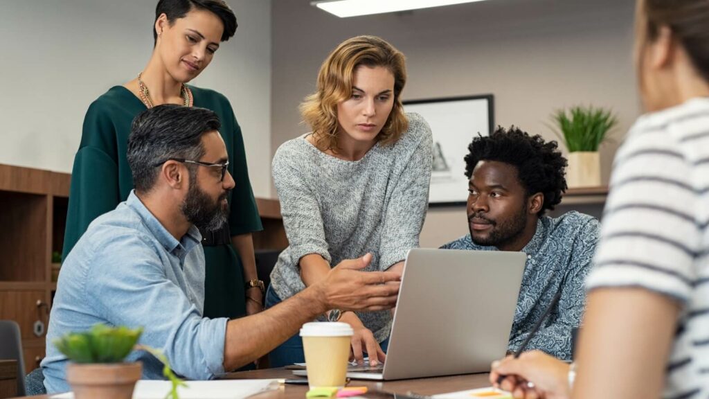 5 diverse adults talking around a labtop